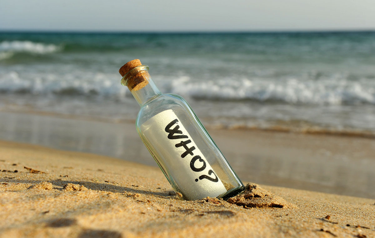 Flaschenpost am Strand mit dem Wort "WHO?" auf der Schriftrolle.